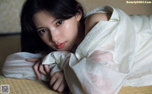 A woman laying on top of a bed covered in a white sheet.