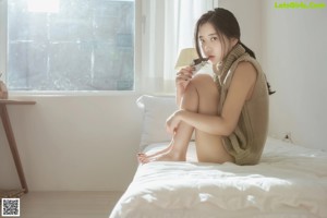 A woman sitting on a window sill eating a piece of chocolate.