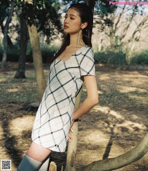 A woman in a pink fur coat leaning against a tree.