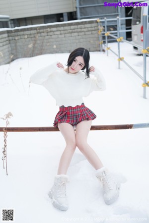 A woman in a white sweater and red plaid skirt posing in the snow.