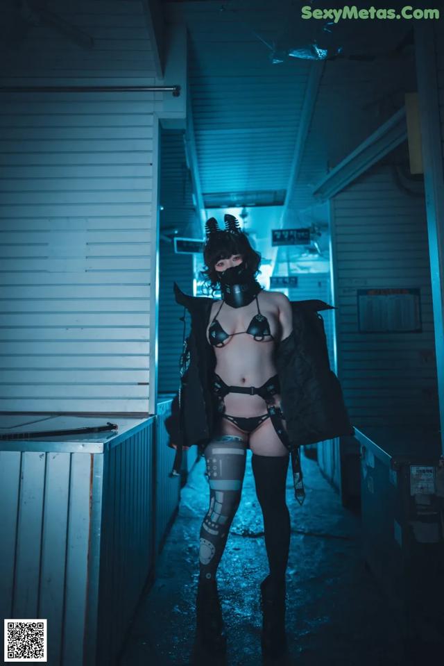 A woman in a black outfit is standing in a dark room.