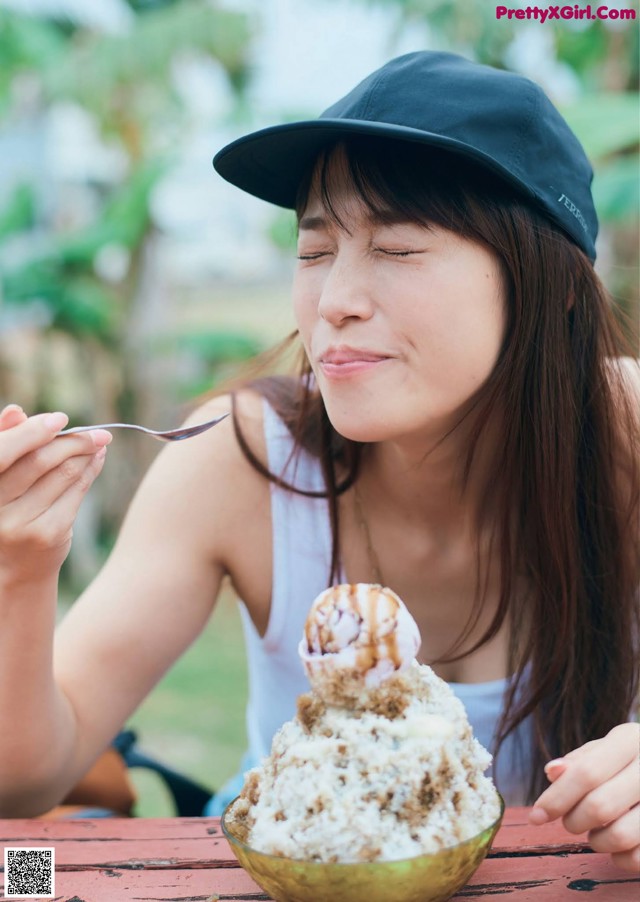 A woman sitting at a table eating an ice cream cone.