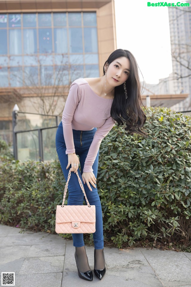 A woman in a pink top and blue jeans posing for a picture.