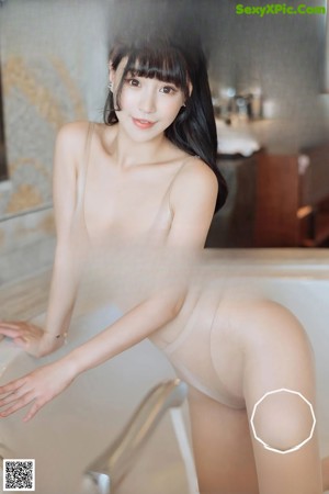 A naked asian woman sitting on a bathtub in a bathroom.