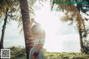 A woman in a bikini standing next to a palm tree.