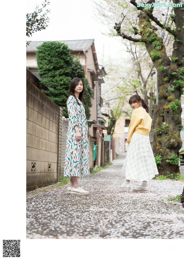 Two women walking down a street next to a tree.