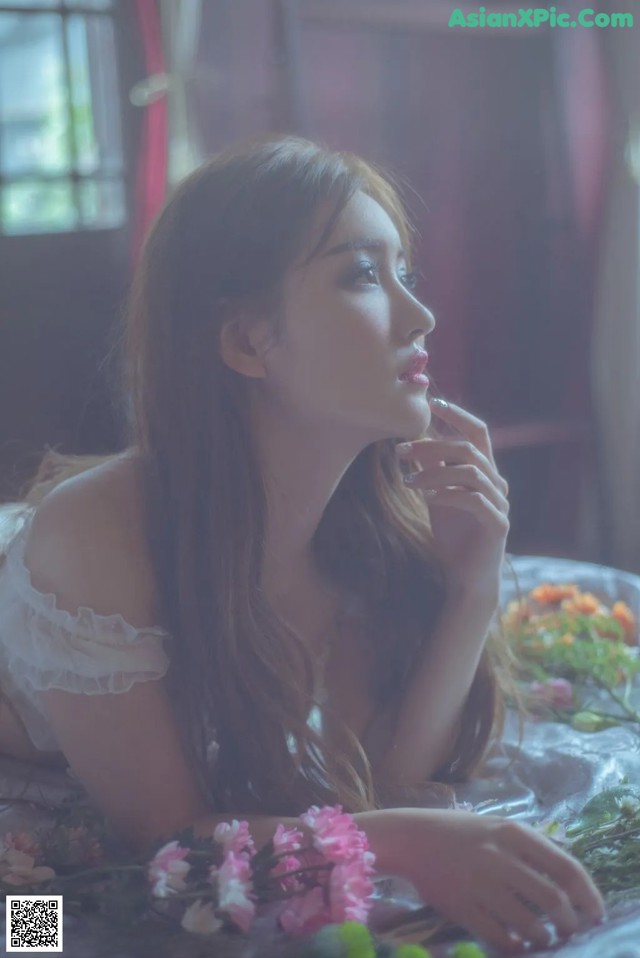 A woman laying on a bed with flowers in her hand.