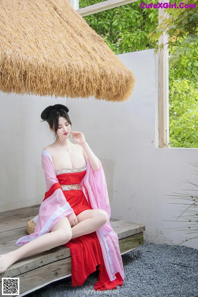 A woman in a red dress sitting on a wooden bench.