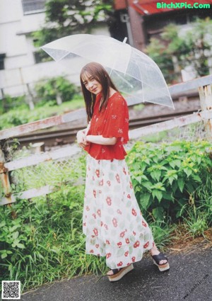 A woman in a red kimono holding an umbrella in a garden.