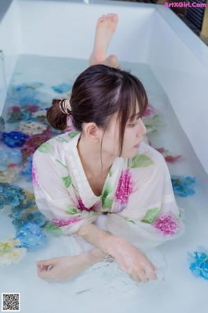 A woman in a bathtub with flowers floating in it.