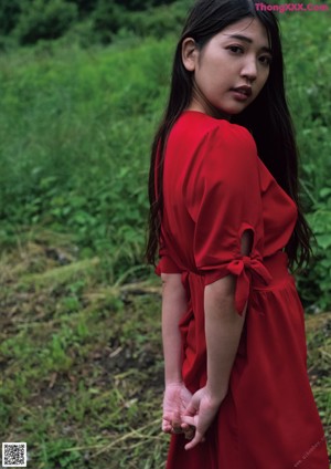 A woman in a red dress sitting on a rock.