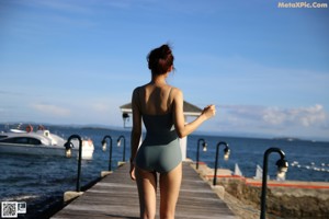 A woman in a black bikini and a baseball cap posing by a pool.