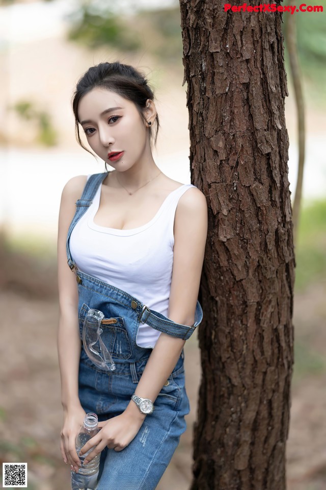 A woman leaning against a tree with a bottle of water.