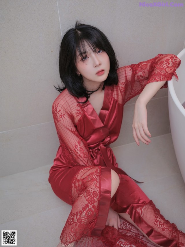 A woman in a red robe sitting on the floor next to a bathtub.