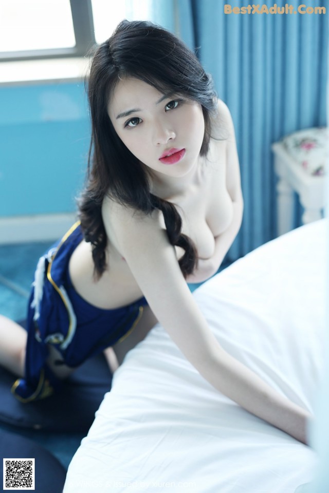 A woman in a blue dress sitting on a bed.