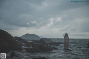 A woman sitting on a concrete wall by the ocean.