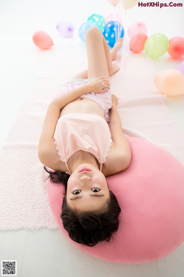 A little girl laying on a pink pillow surrounded by balloons.