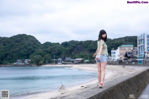 A woman standing on the side of a road next to a beach.