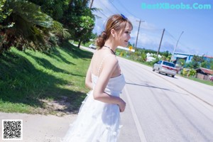 A woman in a white dress standing in front of a bush.