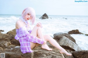 A woman in a bikini sitting on a rock by the ocean.